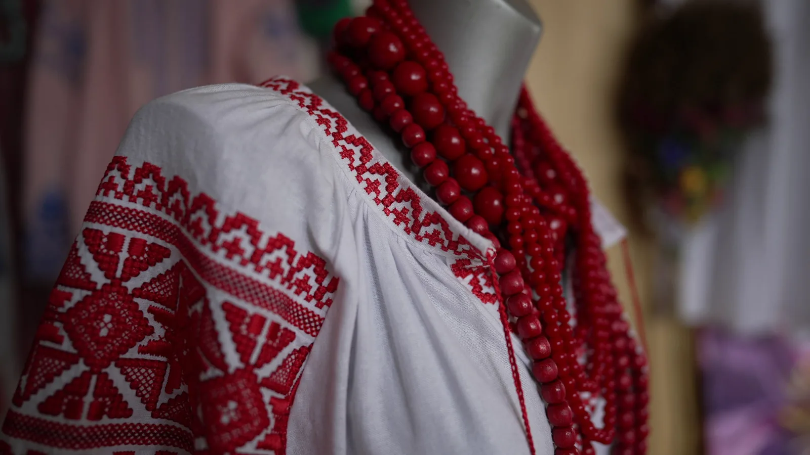 Close-up white dress with red traditional embroidery hanging on mannequin in craft shop. National Ukrainian costume with handmade accessories indoors. Slow motion.